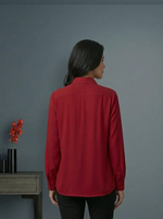 Person wearing a red shirt standing against a gray wall with a small table and decorative items.
