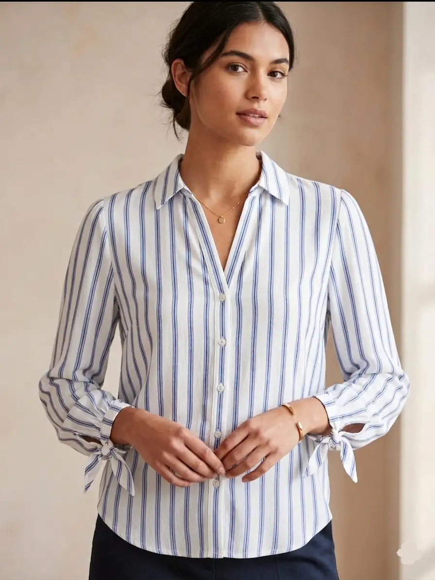 Woman wearing a blue and white striped shirt with long sleeves and tied cuffs.