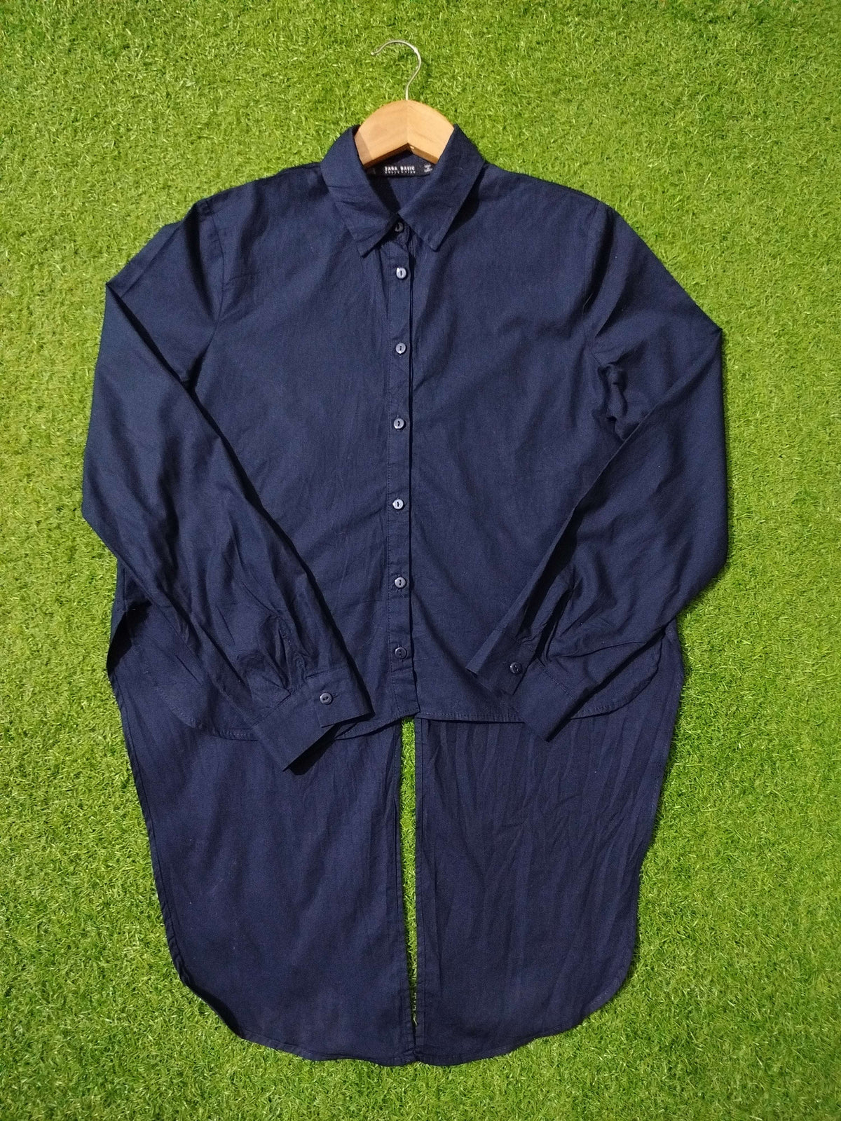 Navy blue shirt on a hanger against a green grass background
