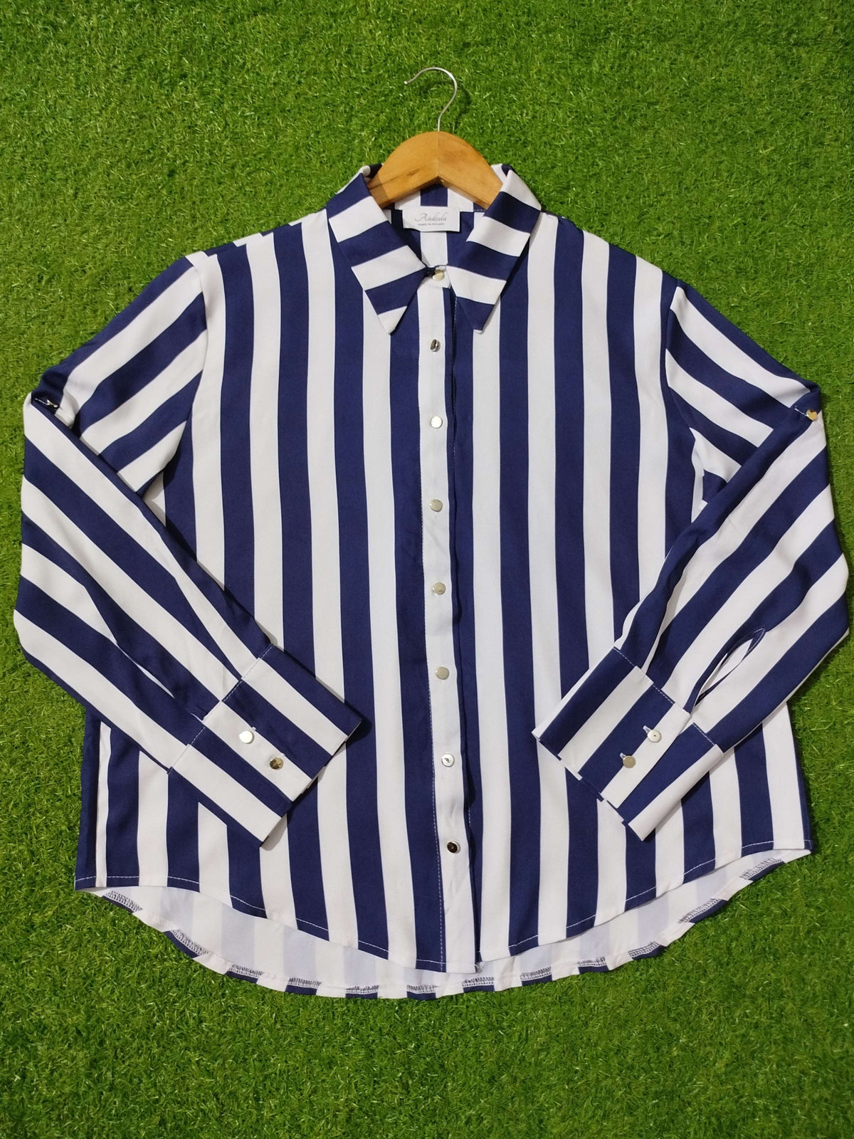 Navy and white striped shirt on a hanger against a green grass background
