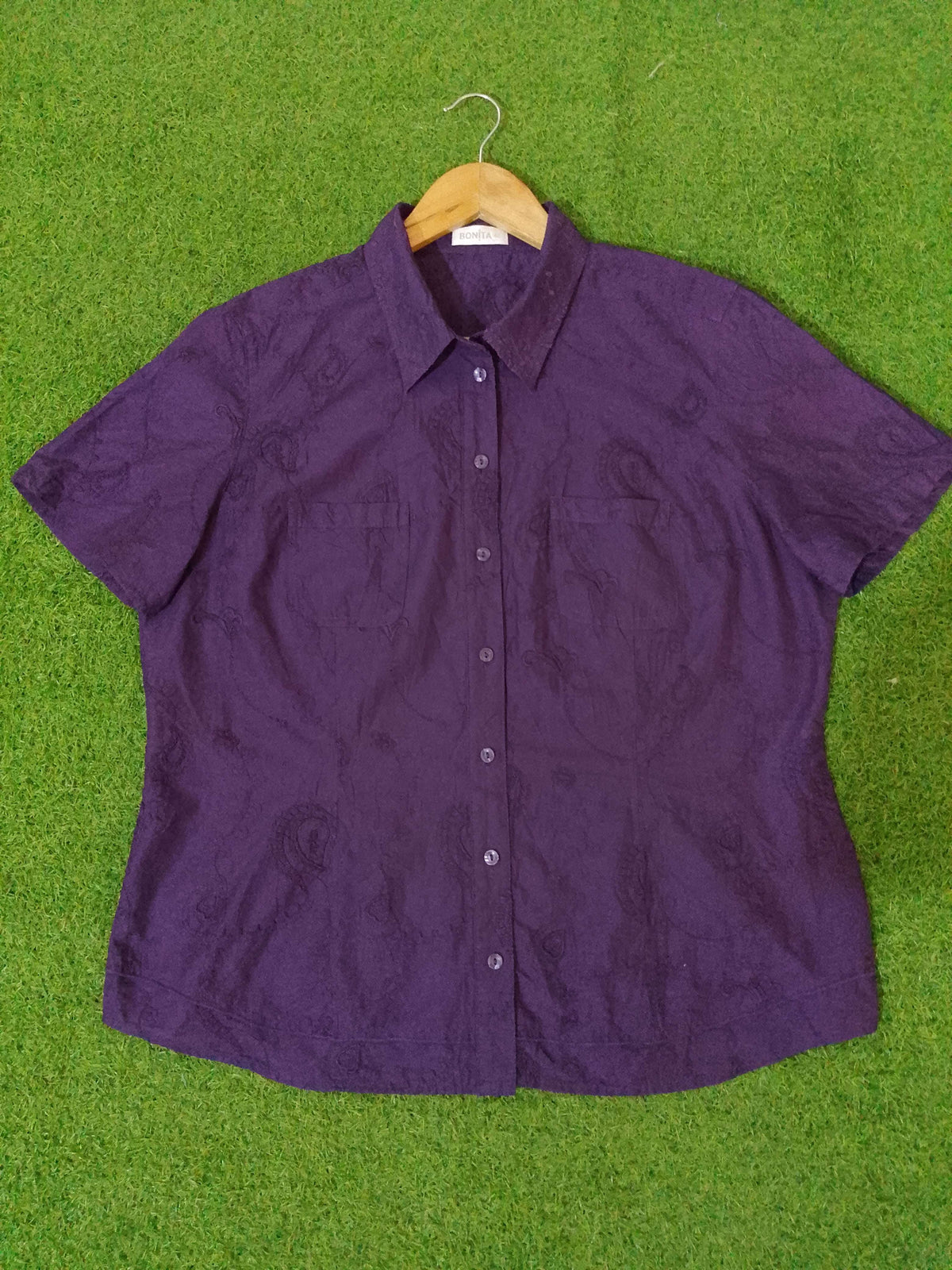 Purple short-sleeve shirt on a wooden hanger against a green grass background