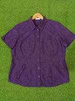 Purple short-sleeve shirt on a wooden hanger against a green grass background