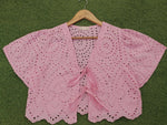 Pink crochet top on a wooden hanger against a green background