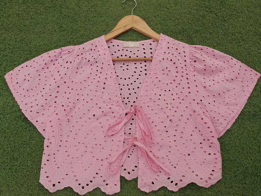 Pink crochet top on a wooden hanger against a green background - alternate view