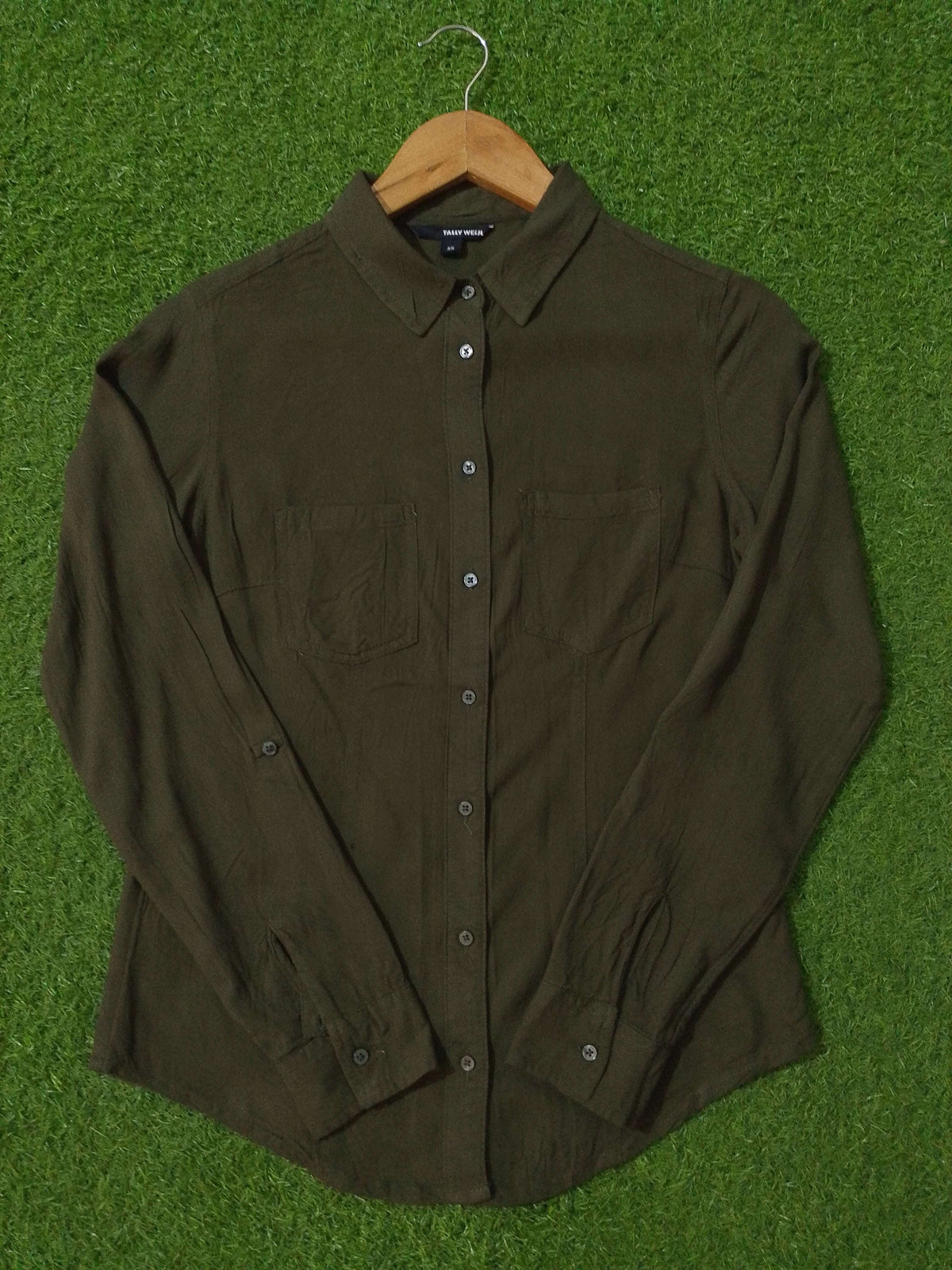 Dark green shirt on a wooden hanger against a green grass background