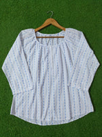 White blouse with blue patterns on a wooden hanger against a green background