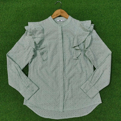 Green blouse with ruffled sleeves on a hanger against a green background