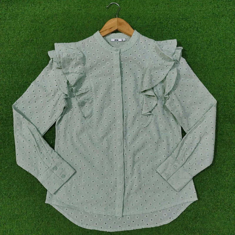 Green blouse with ruffled sleeves on a hanger against a green background