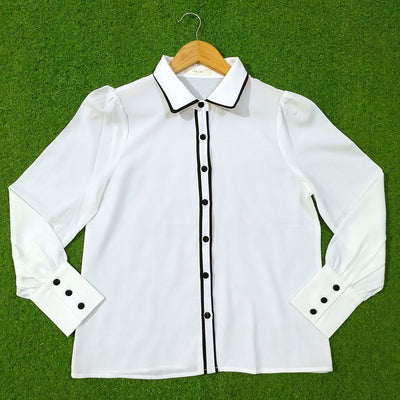White blouse with black accents on a hanger against a green background