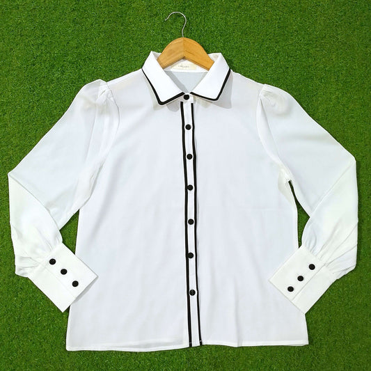 White blouse with black accents on a hanger against a green background