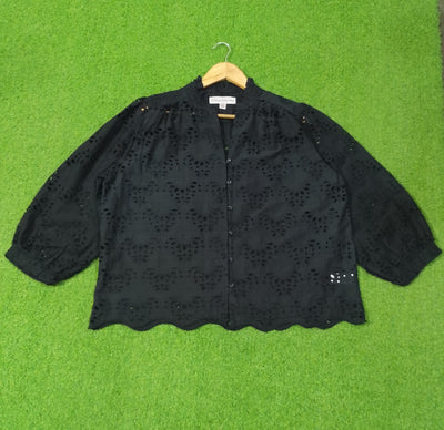 Black lace blouse on a hanger against a green background