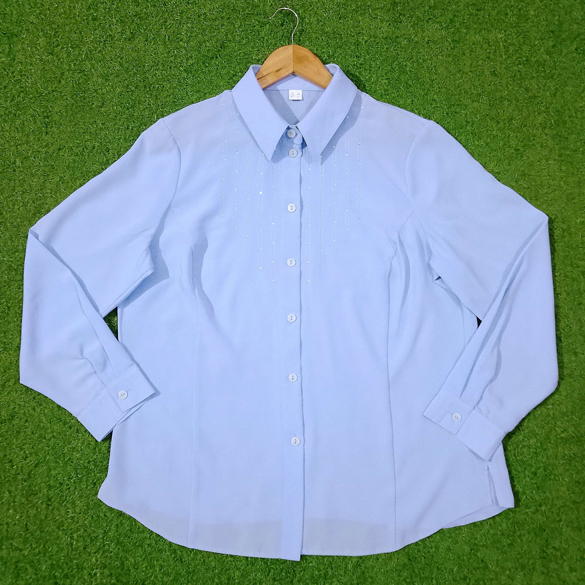 Light blue button-up shirt on a wooden hanger against a green grass background