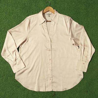 A light beige long-sleeve button-up shirt with a pointed collar, laid flat on a green artificial turf background and hanging on a wooden hanger.