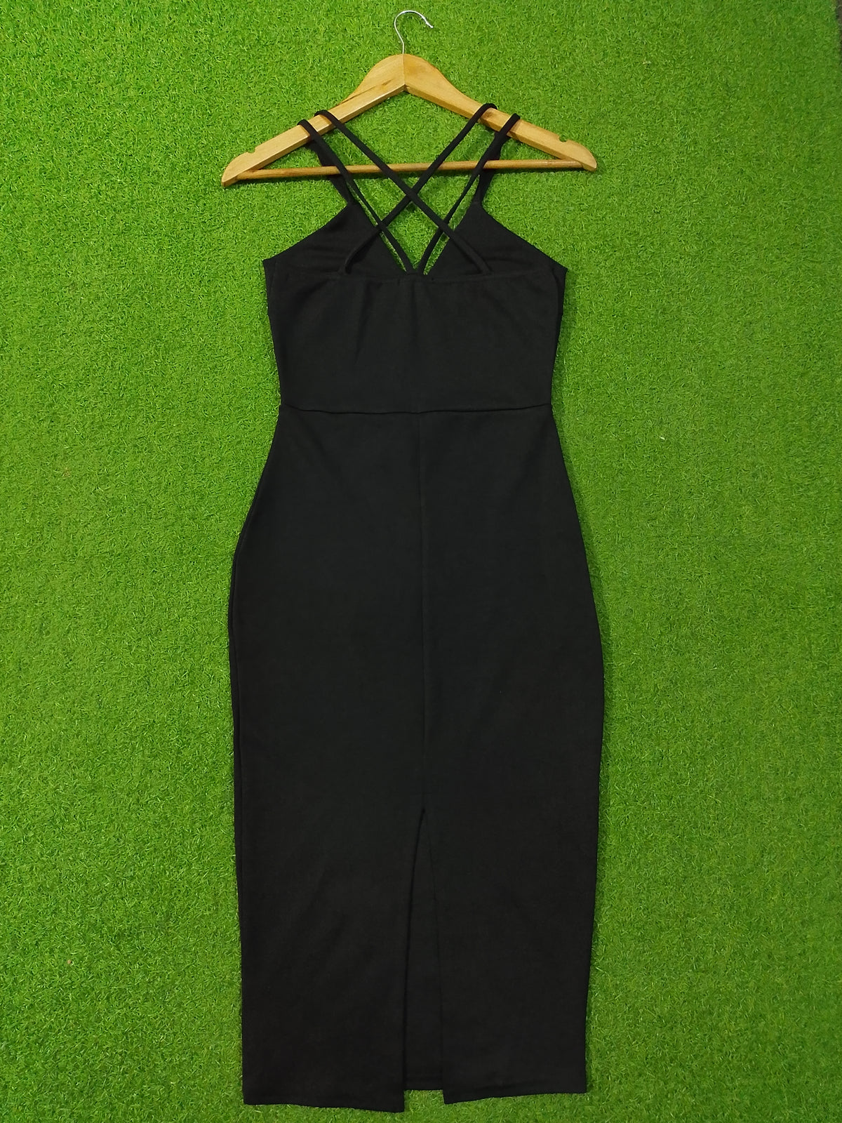 A black sleeveless bodycon dress with crisscross shoulder straps, hanging on a wooden hanger against a bright green artificial grass background.