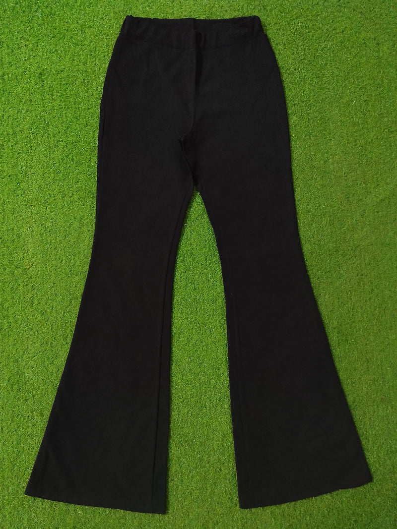 Black flared pants laid flat on a bright green grass-like background.