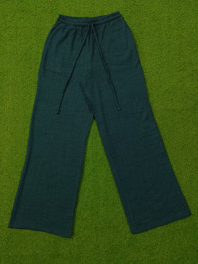 Dark teal wide-leg lounge pants with a textured waffle fabric and drawstring waist, laid flat on a green artificial turf background.