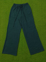 Dark teal wide-leg lounge pants with a textured waffle fabric and drawstring waist, laid flat on a green artificial turf background.