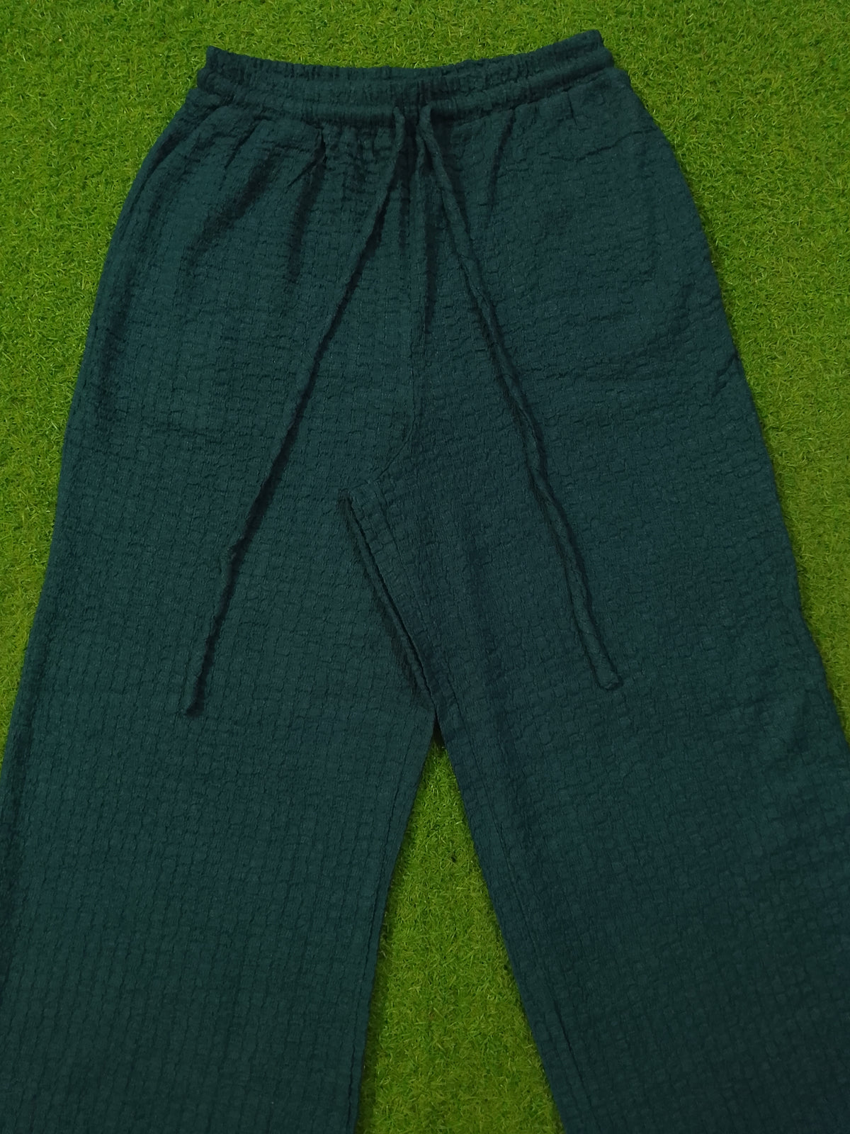 Dark green textured lounge pants with an elastic drawstring waist, laid flat on a green grass-like surface.