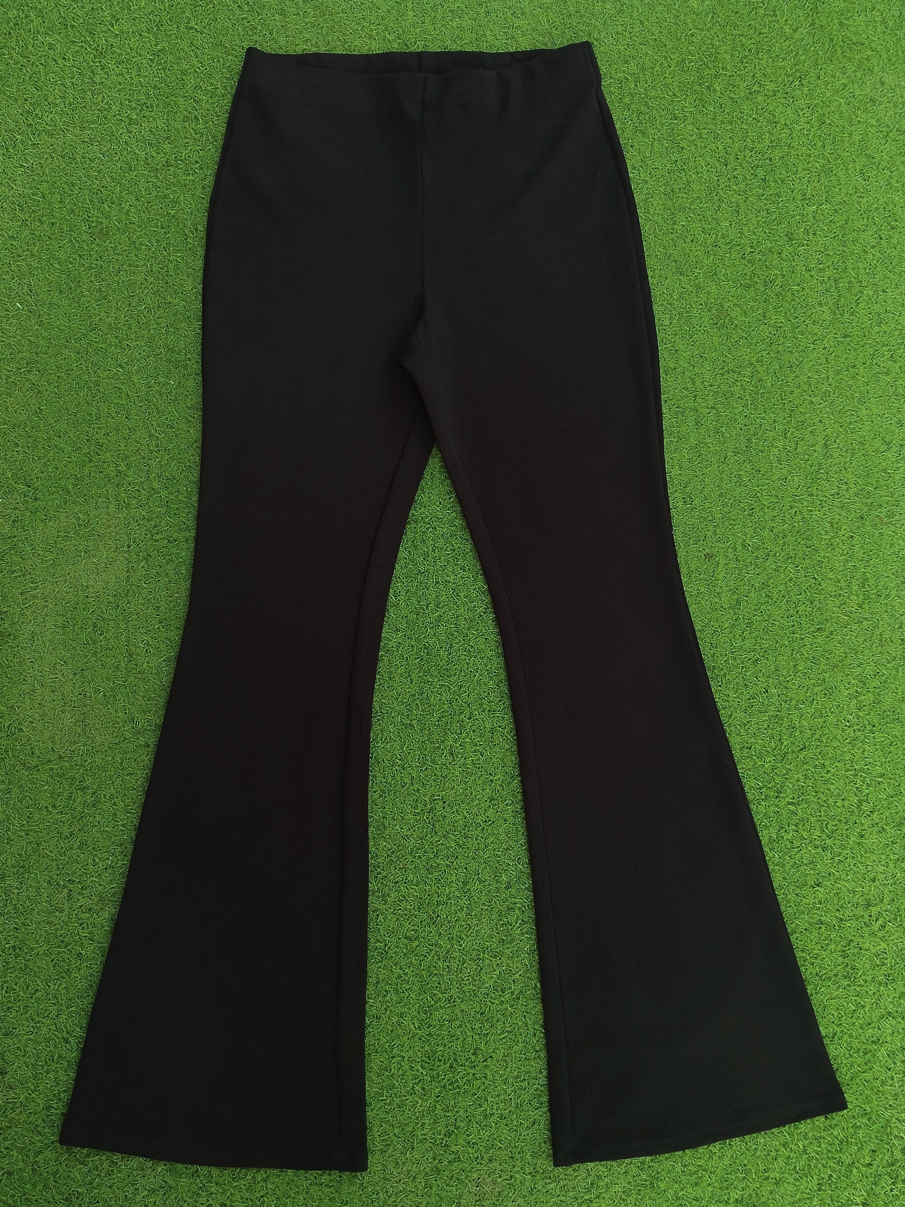 Black flare pants laid flat on a bright green textured background.