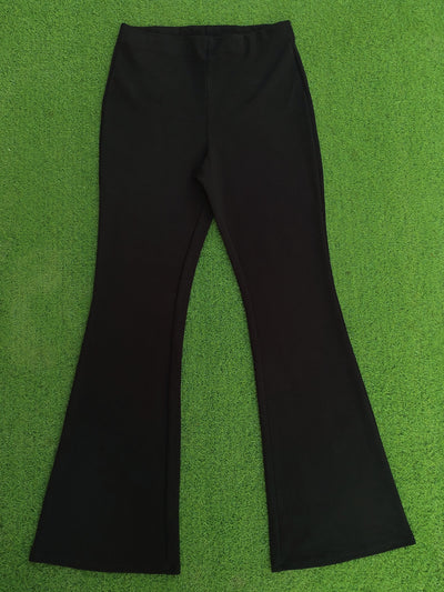 Black flare pants laid flat on a bright green textured background.