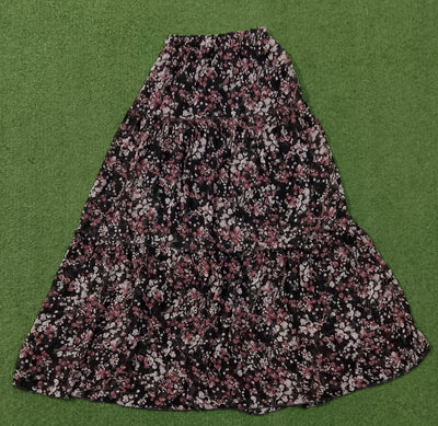 A black midi skirt with a dense pink and white floral print, laid flat on a green textured background. - alternate view