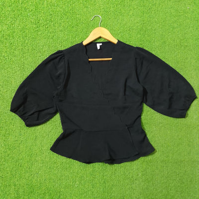 A black long-sleeve top or jacket laid flat on a bright green artificial grass surface, hanging from a wooden hanger.