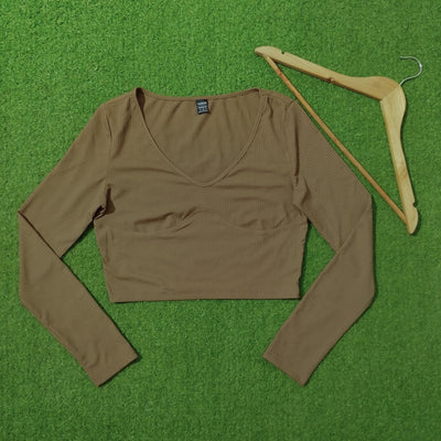 A brown ribbed long-sleeve crop top laid flat on a green grass-like surface next to a wooden hanger. - alternate view