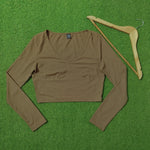 A brown ribbed long-sleeve crop top laid flat on a green grass-like surface next to a wooden hanger.