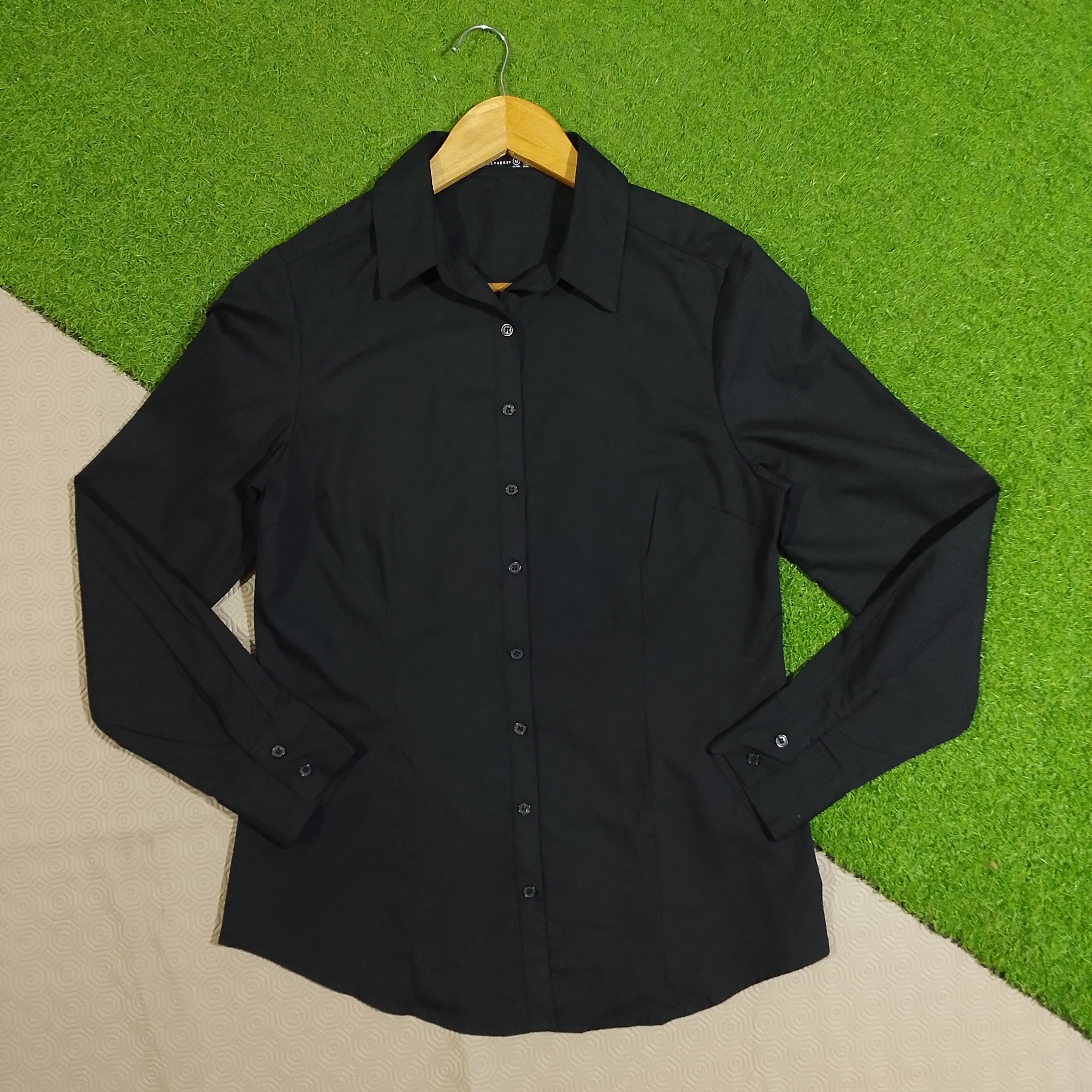 Black collared button-down shirt with full sleeves on a wooden hanger