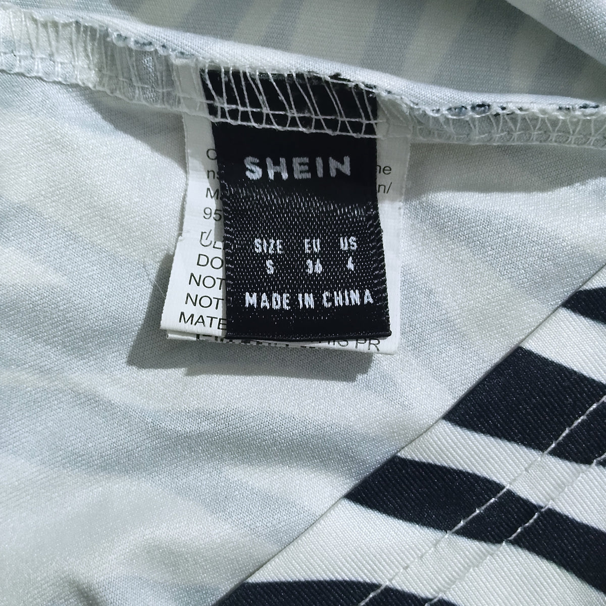 Close-up of a garment's inner neck label reading SHEIN, with size information visible on a white and navy striped fabric.