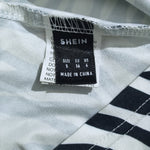 Close-up of a garment's inner neck label reading SHEIN, with size information visible on a white and navy striped fabric.