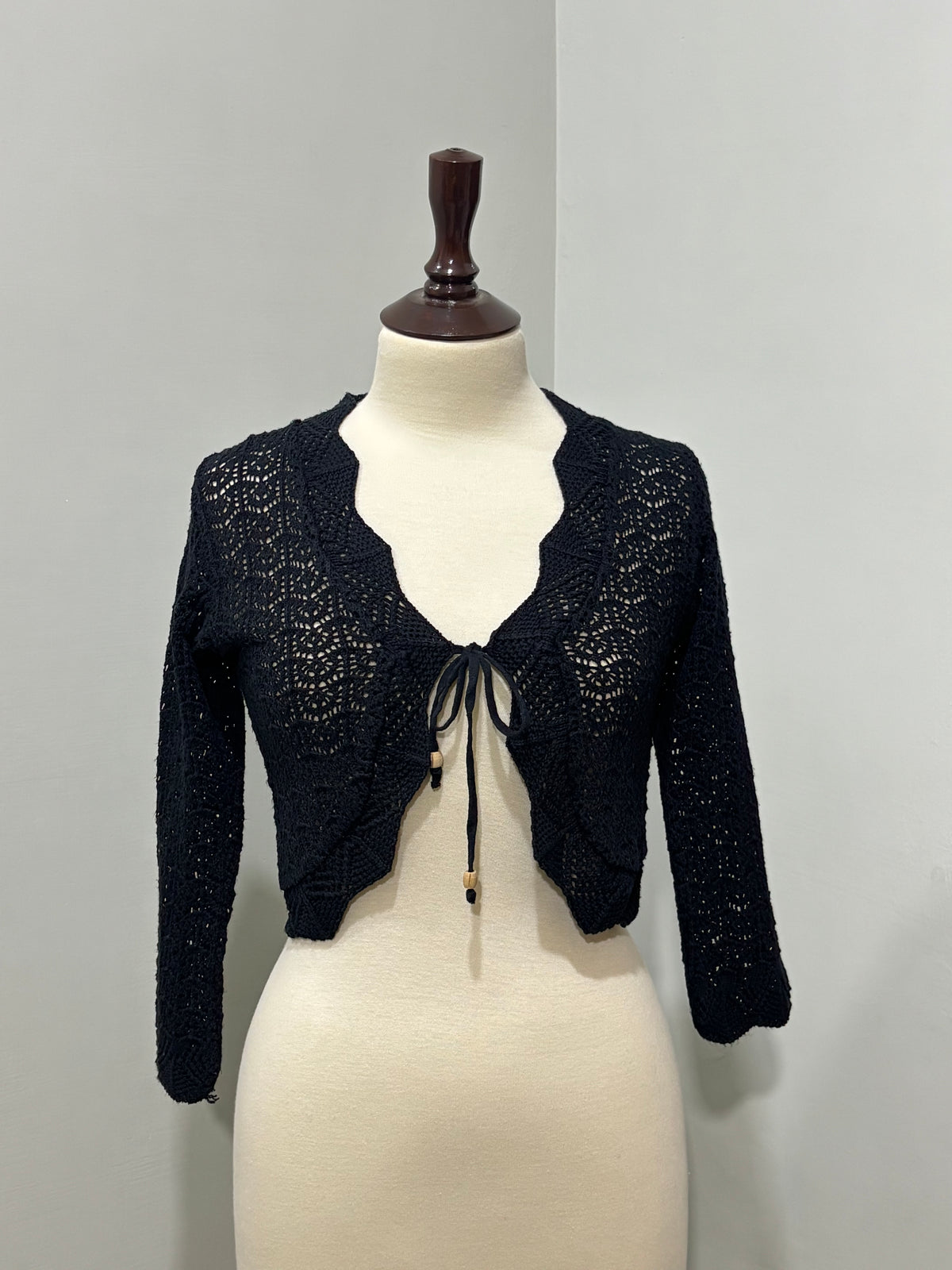 Black openwork cropped cardigan with scalloped edges, long sleeves and beaded front ties