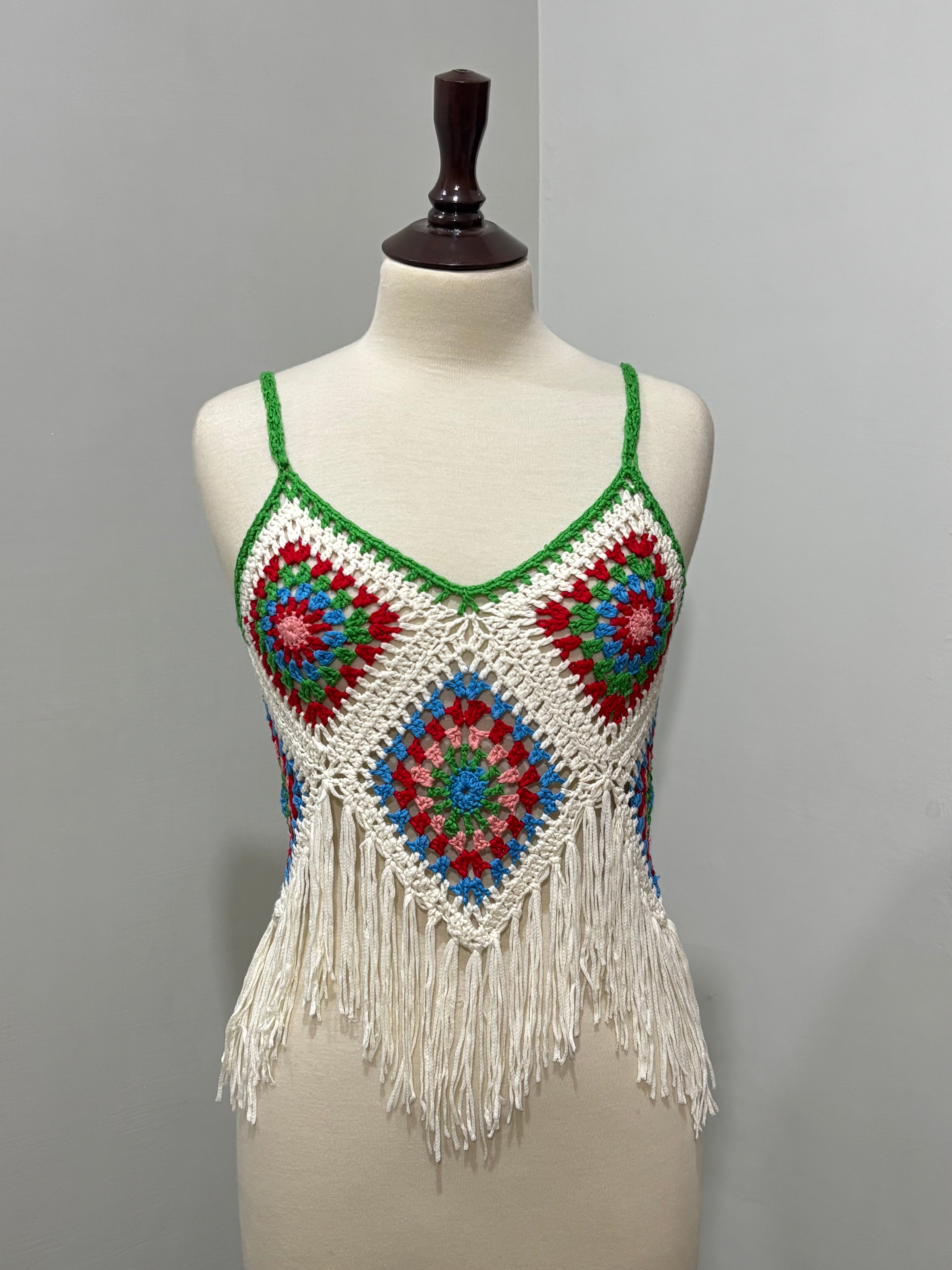Front of cream and multicolor floral crochet strappy top with green trim and fringe hem