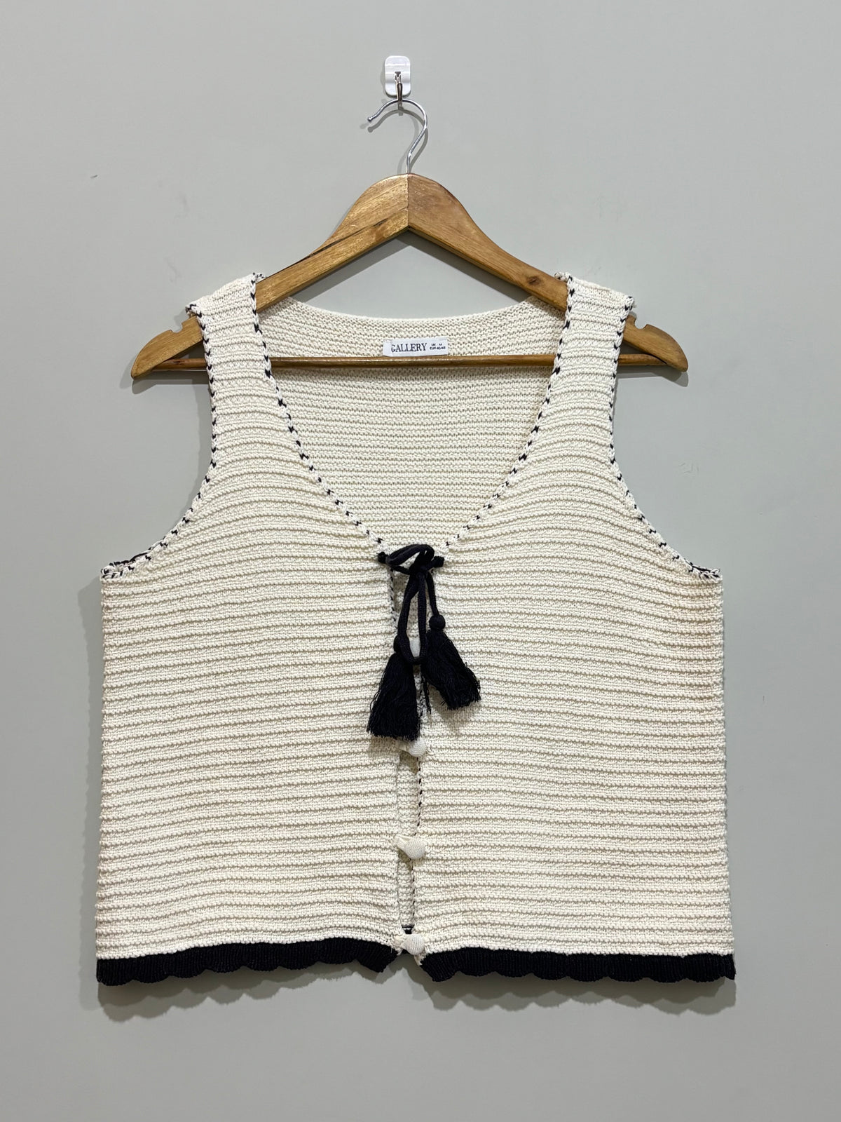 Cream and black textured sleeveless vest with tassel tie, buttons and scalloped hem