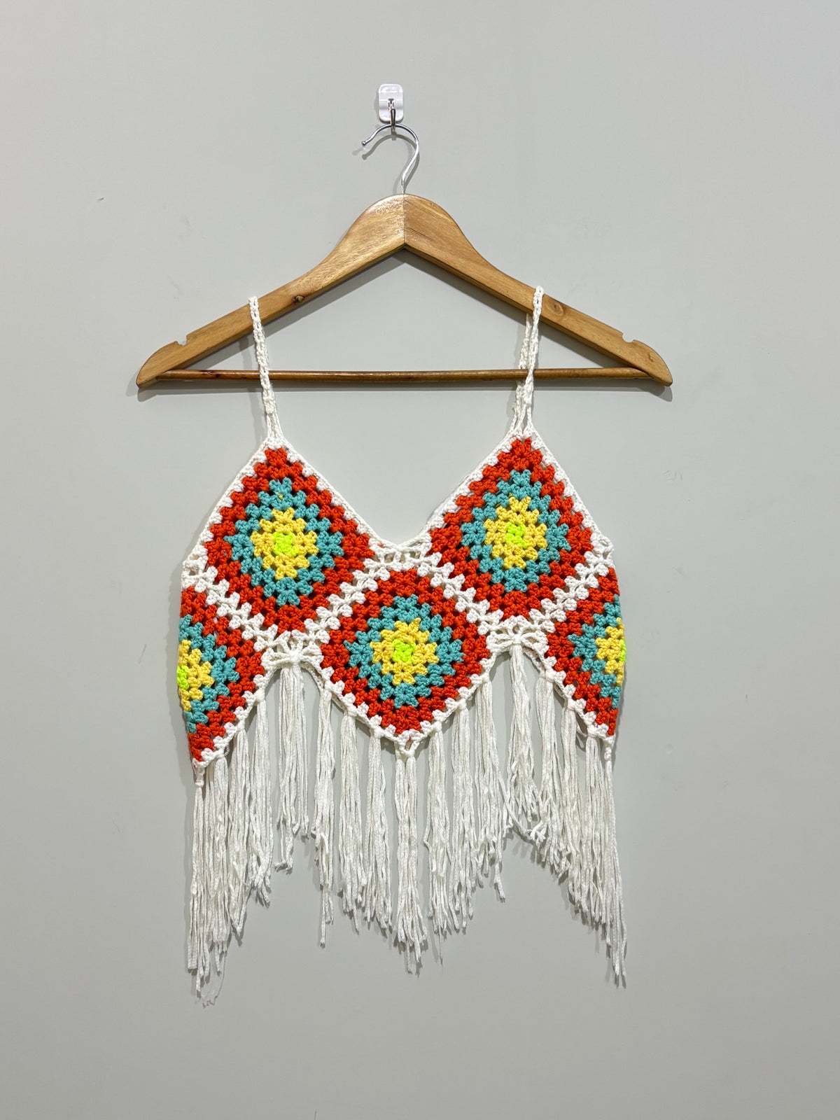 White and orange crochet crop top with yellow and turquoise motifs on hanger
