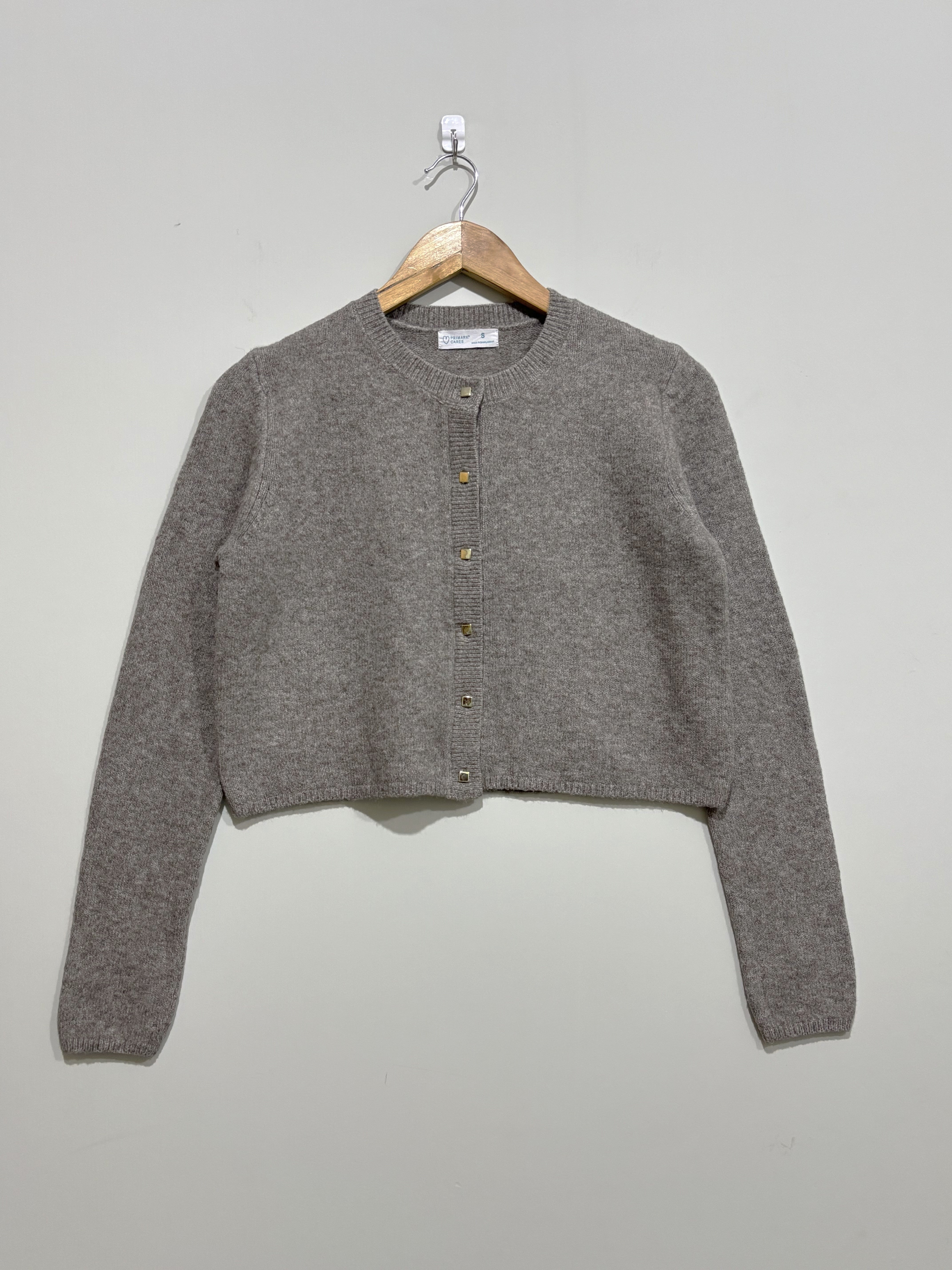 Grey cropped round-neck cardigan with front buttons, long sleeves and ribbed neckline, cuffs and hem, on a wooden hanger.