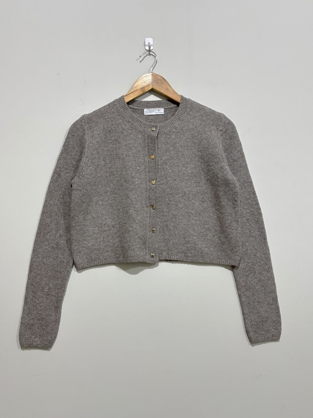 Grey cropped round-neck cardigan with front buttons, long sleeves and ribbed neckline, cuffs and hem, on a wooden hanger.