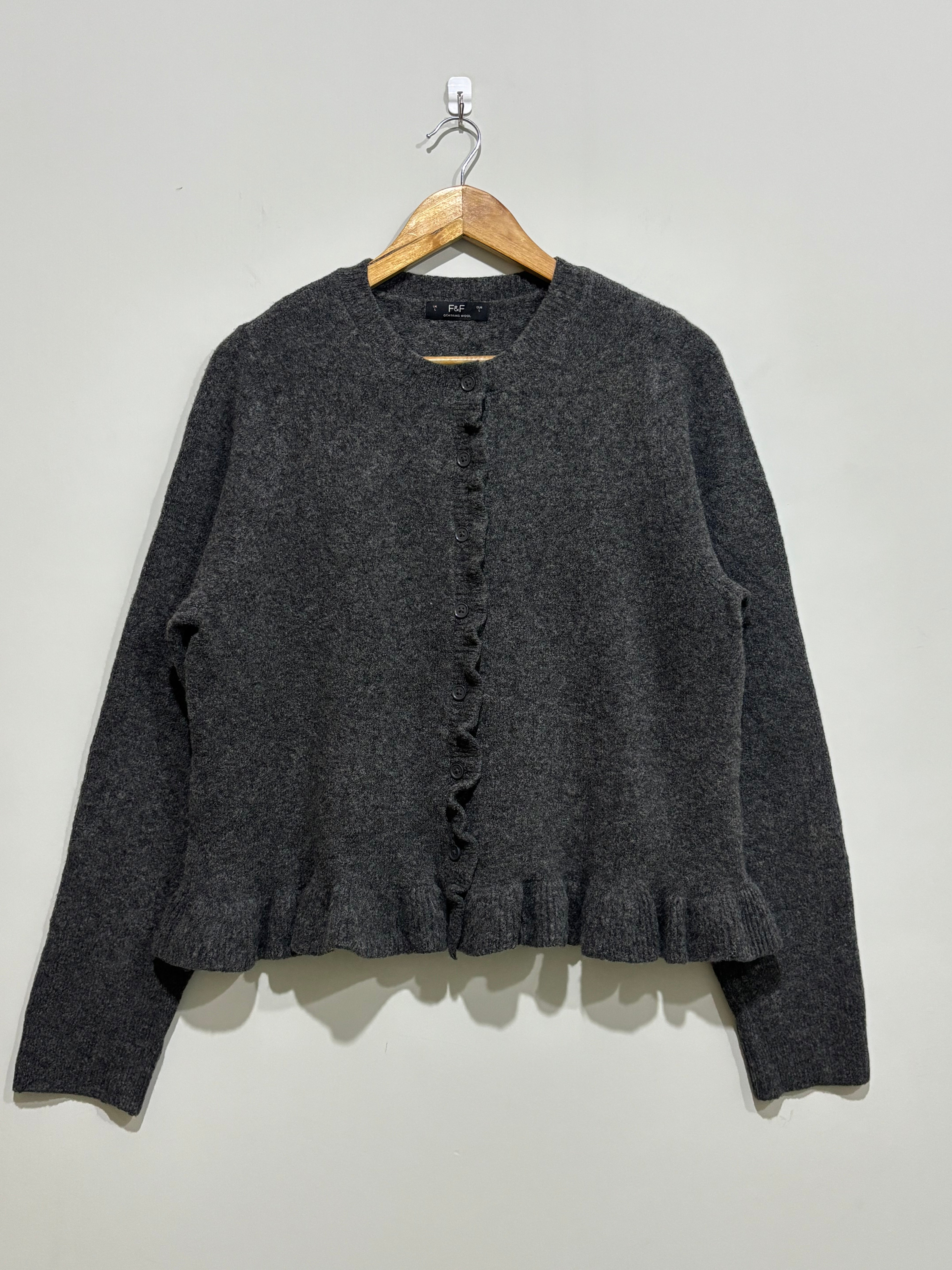 Charcoal grey round-neck cardigan with long sleeves, a ruffled button-front placket and ruffle hem.