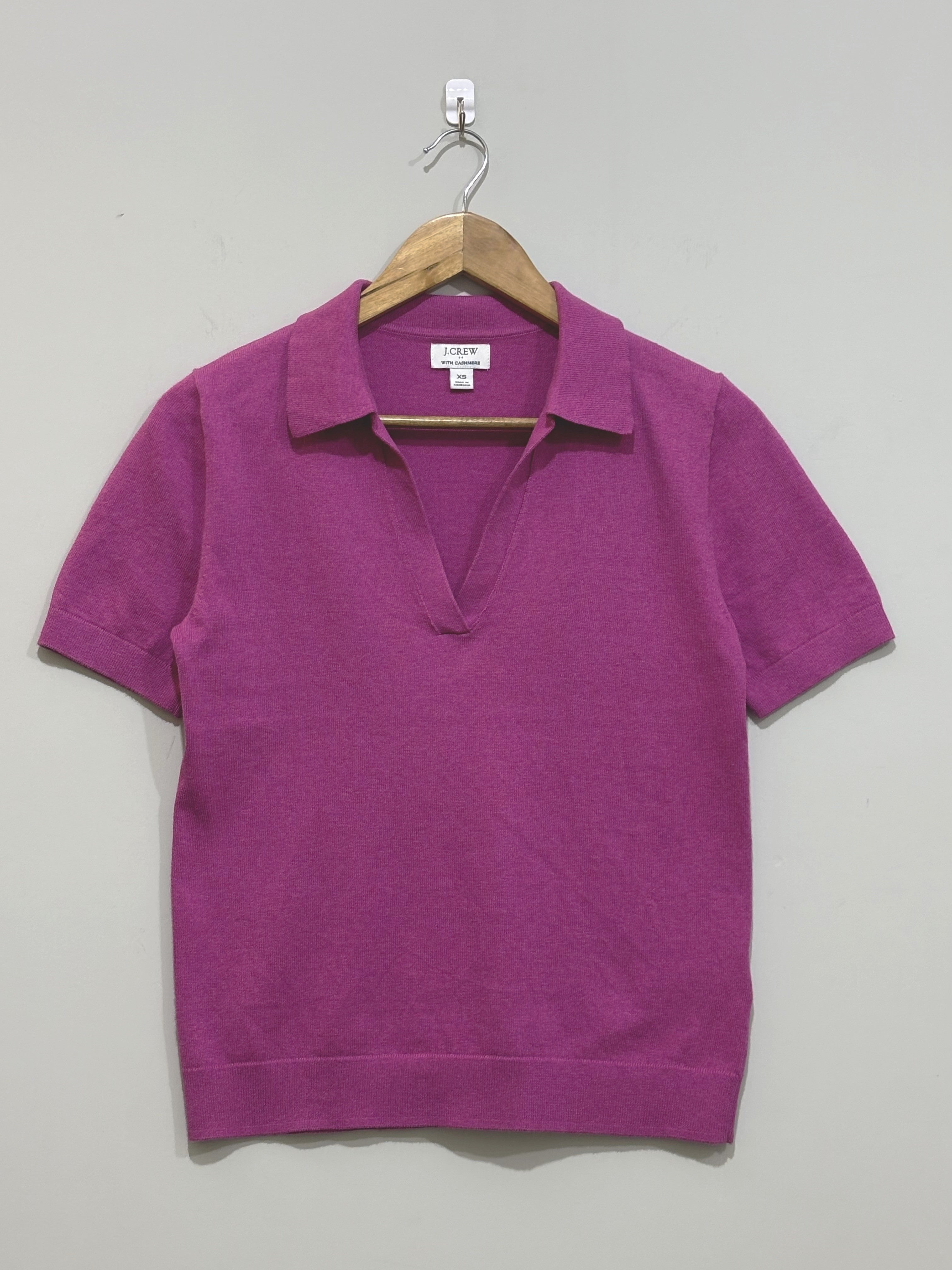 Magenta short-sleeve top with a pointed collar, open V-neckline and ribbed cuffs and hem, shown on a wooden hanger.