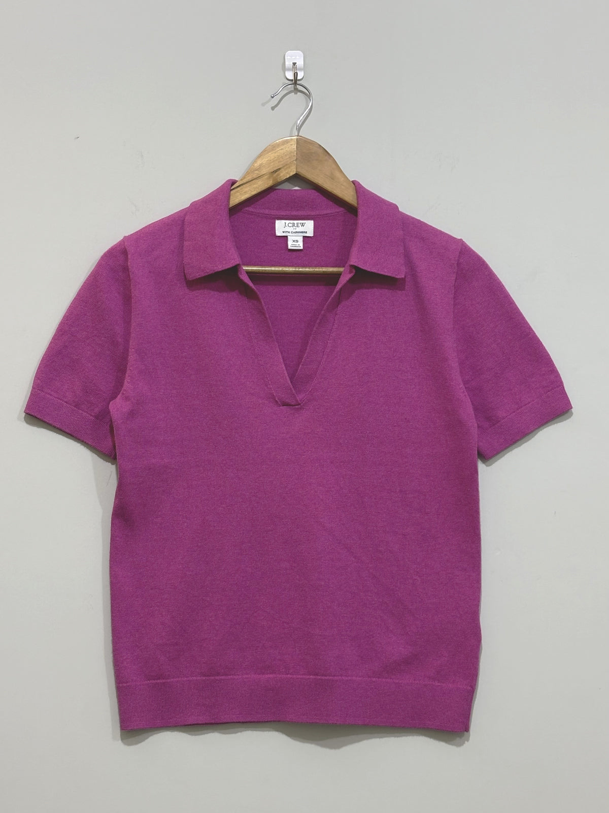 Magenta short-sleeve top with a pointed collar, open V-neckline and ribbed cuffs and hem, shown on a wooden hanger.