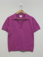 Magenta short-sleeve top with a pointed collar, open V-neckline and ribbed cuffs and hem, shown on a wooden hanger.