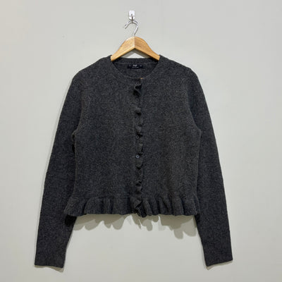 Charcoal grey long-sleeve cardigan with a round neckline, ruffled button-front trim and ruffle hem on a wooden hanger.