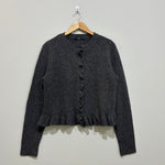 Charcoal grey long-sleeve cardigan with a round neckline, ruffled button-front trim and ruffle hem on a wooden hanger.