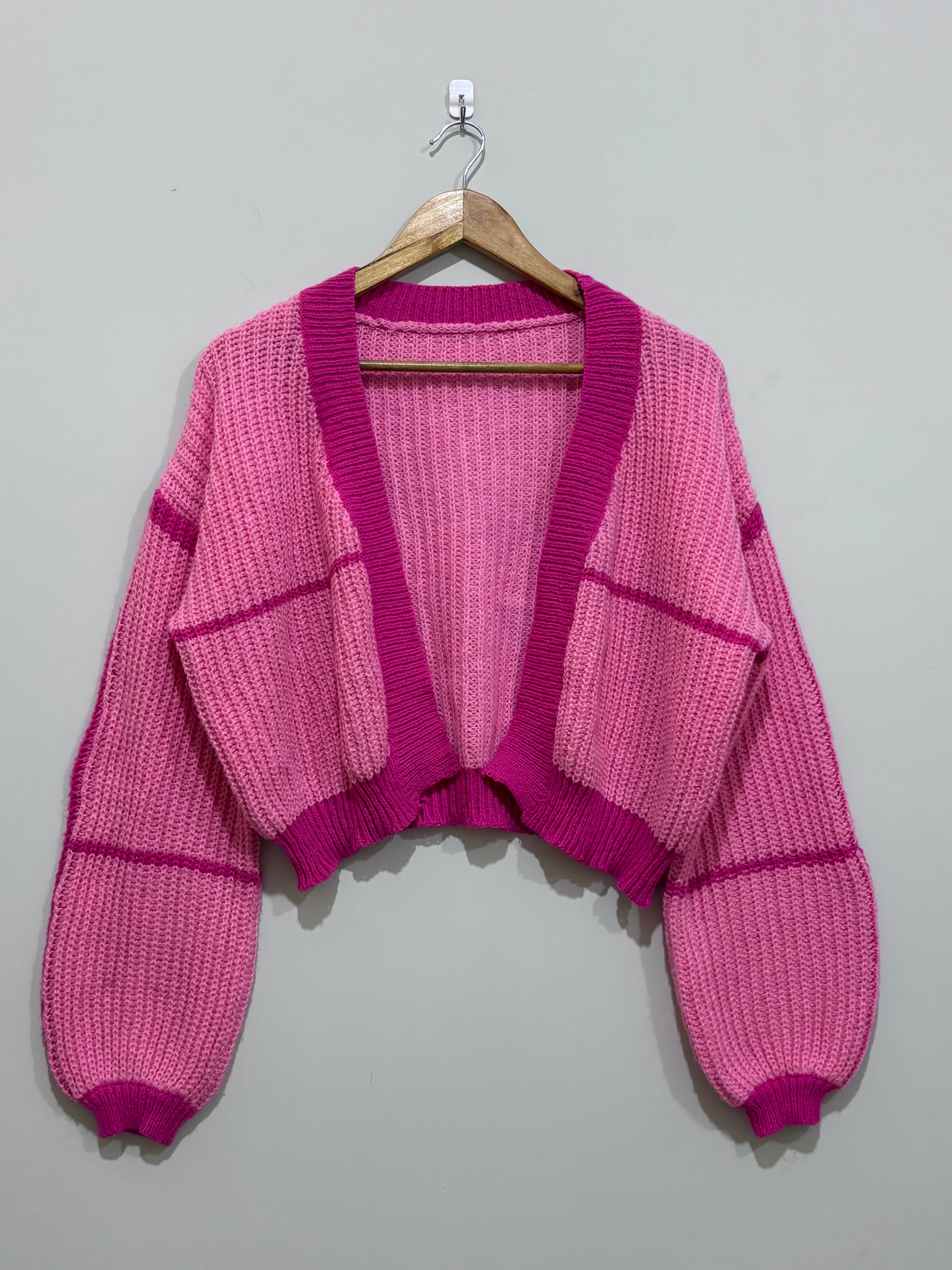 Pink cropped open-front knit cardigan with magenta contrast ribbed trim, drop shoulders and voluminous long sleeves.