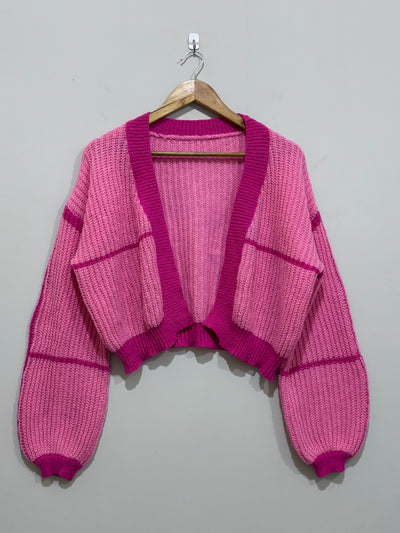 Pink cropped open-front knit cardigan with magenta contrast ribbed trim, drop shoulders and voluminous long sleeves.
