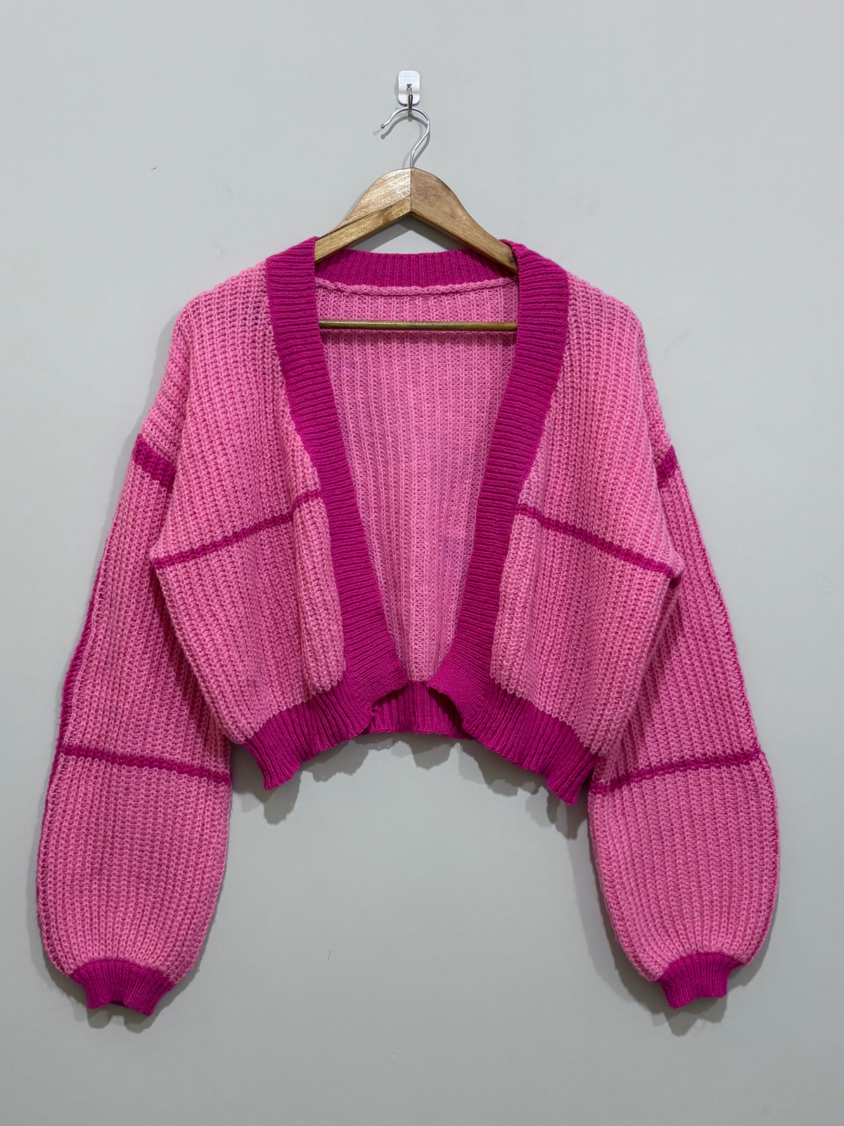Pink cropped open-front knit cardigan with magenta contrast ribbed trim, drop shoulders and voluminous long sleeves.