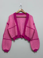 Pink cropped open-front knit cardigan with magenta contrast ribbed trim, drop shoulders and voluminous long sleeves.