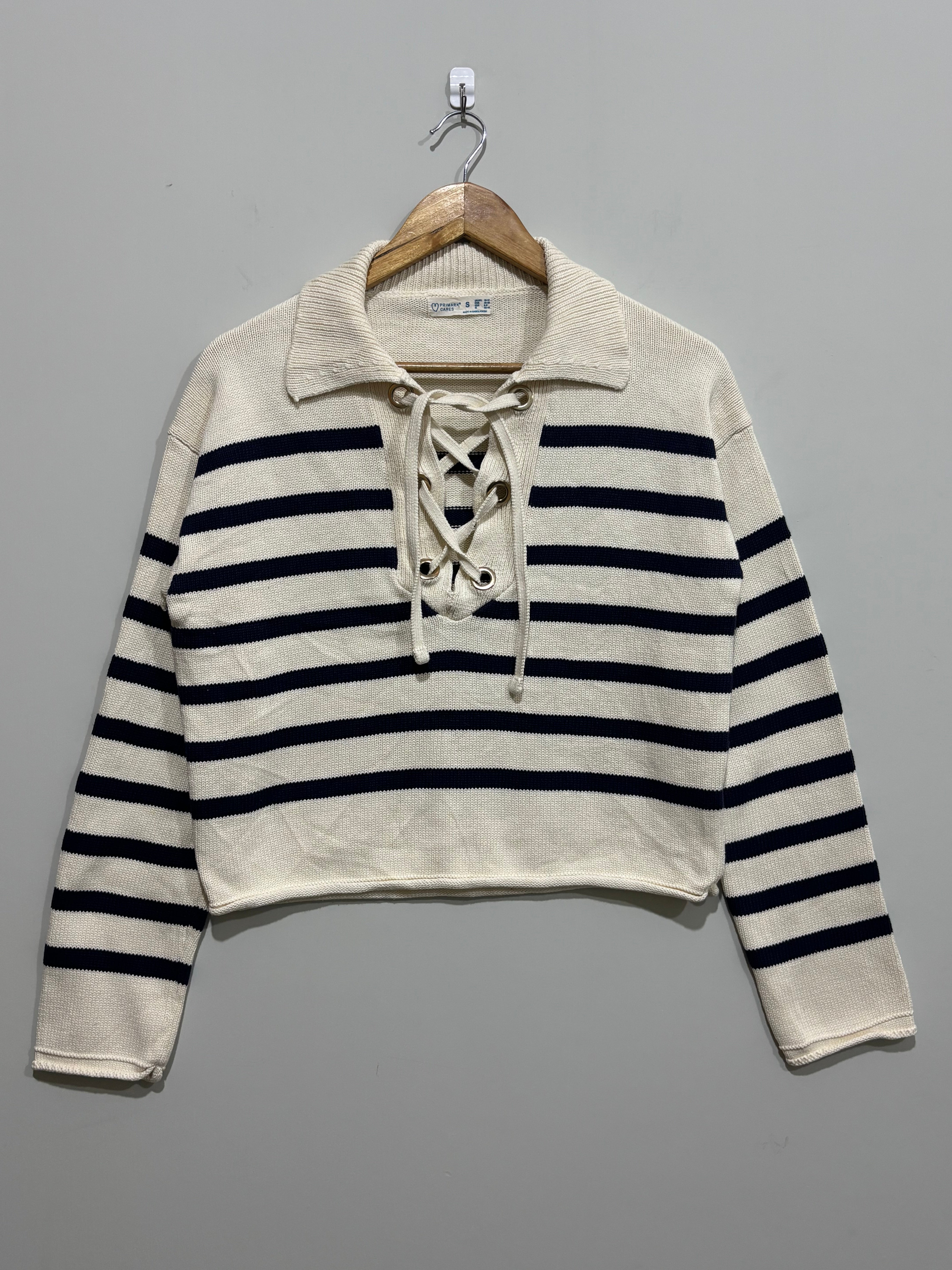 Cream and black horizontally striped cropped blouse with a wide collar, lace-up neckline and long drop-shoulder sleeves on a hanger.