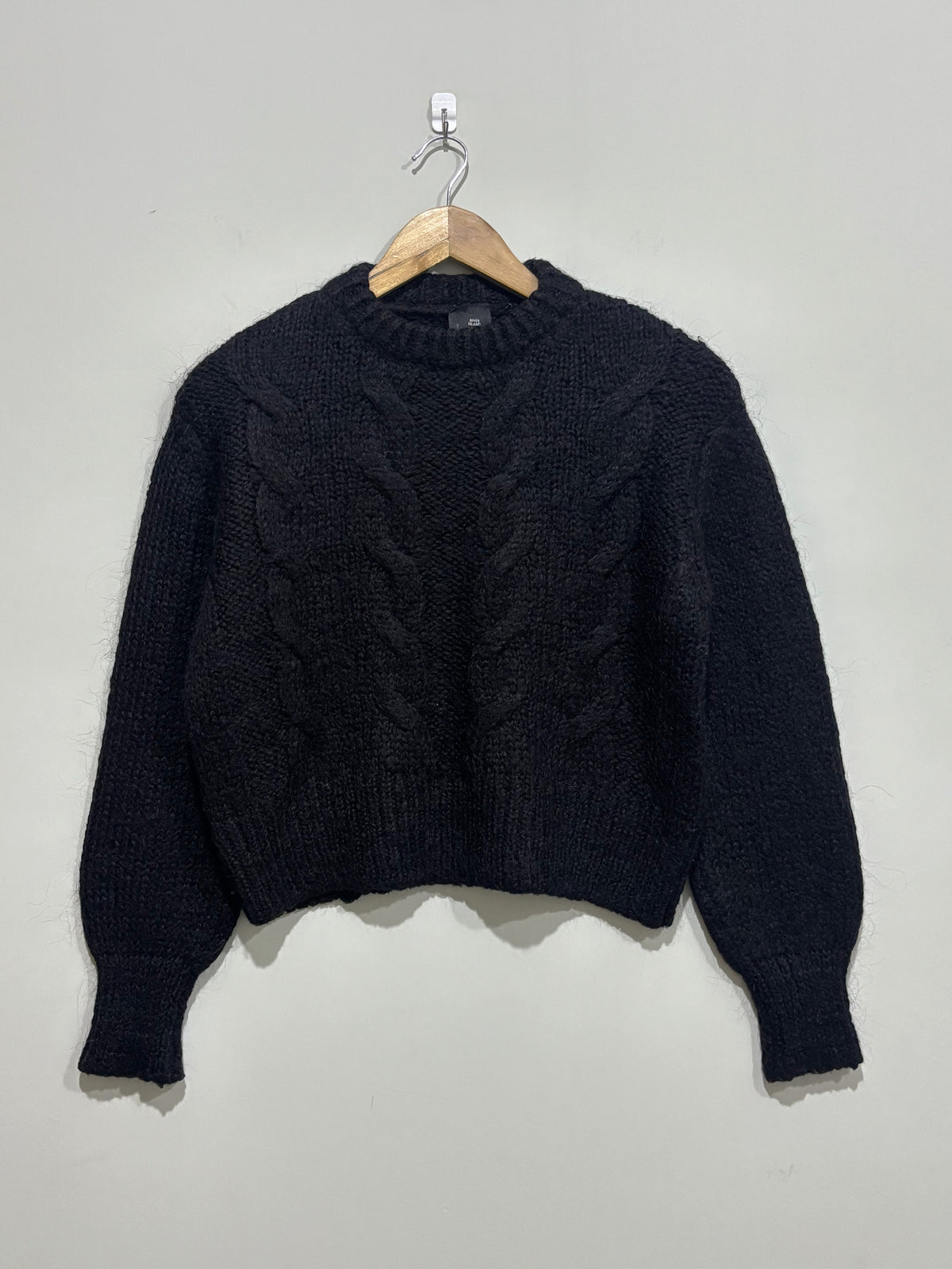 Black cable-knit pullover with a crew neckline, full balloon sleeves and ribbed cuffs and hem on a wooden hanger.