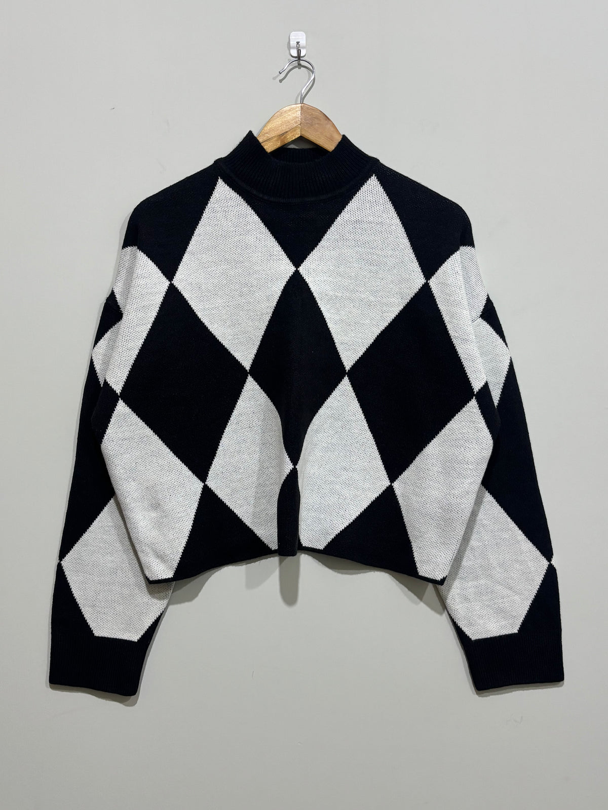 Black and white oversized diamond-pattern knitted blouse with a high neckline, dropped shoulders and long sleeves.
